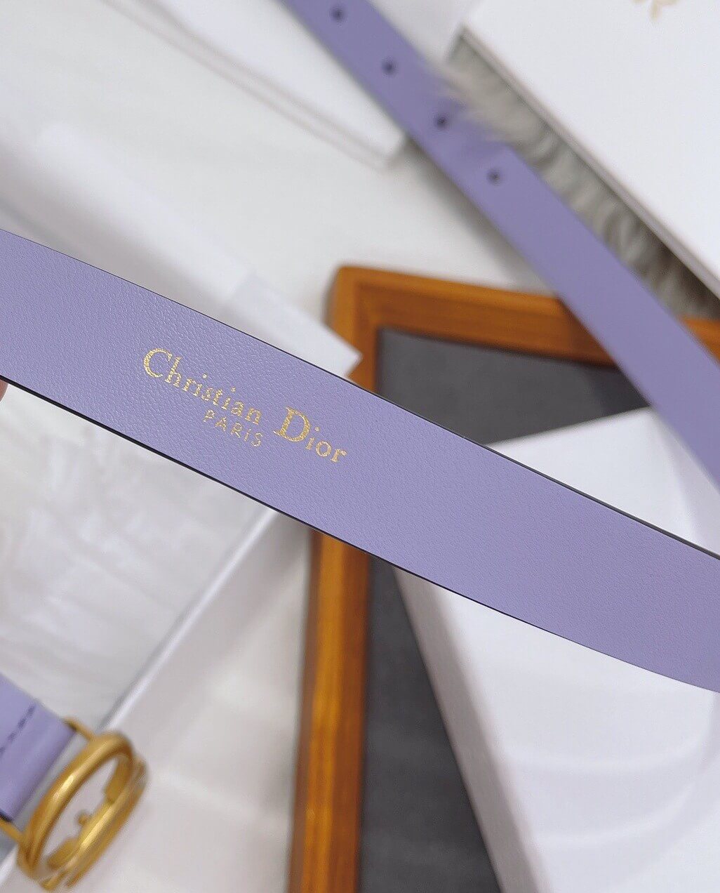 Close-up of a purple Christian Dior belt with gold hardware on a white background.