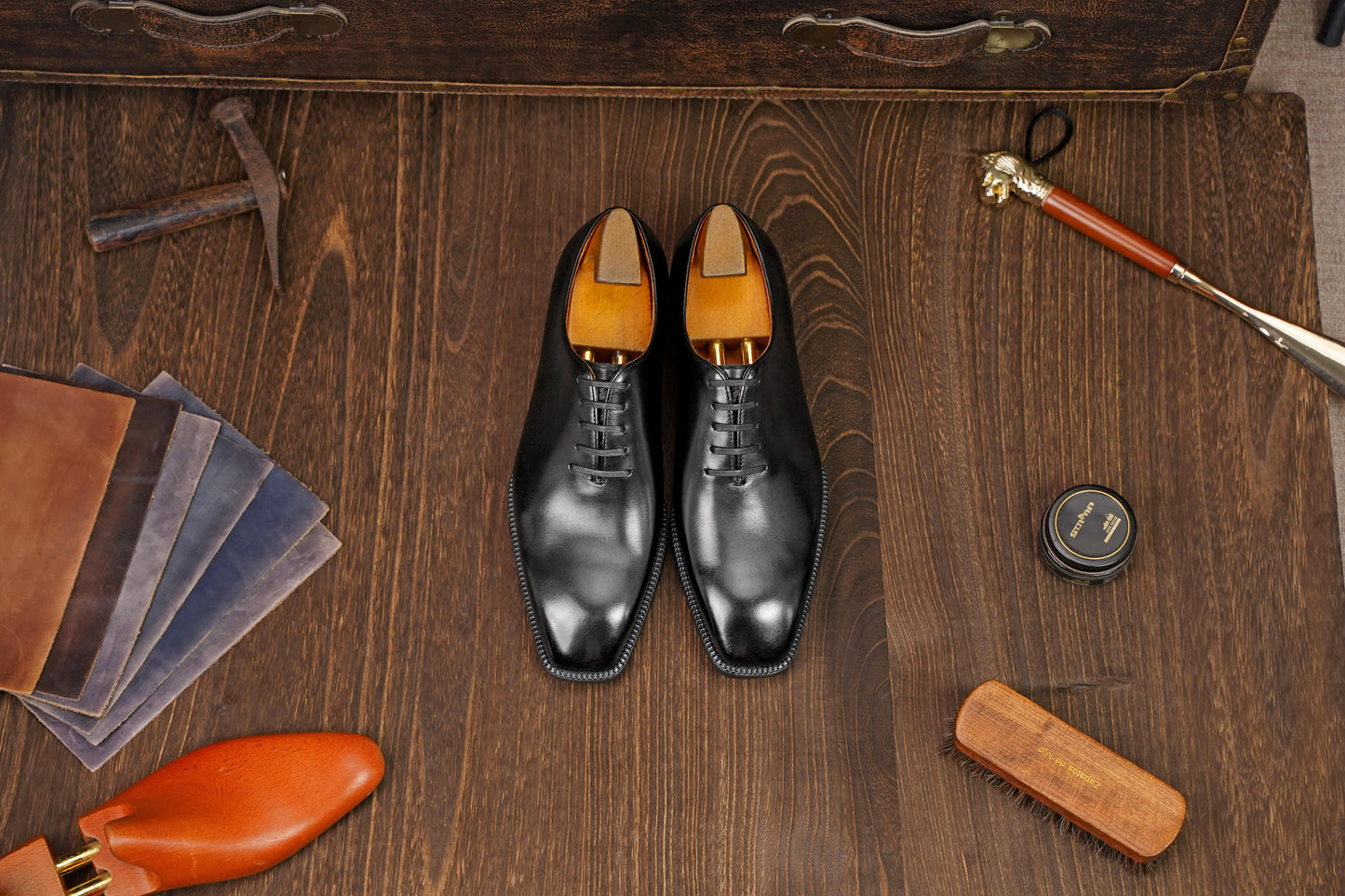 Classic Black Leather Wholecut Oxford Dress Shoes – a flat-lay, top-down view of the formal footwear on a rustic wooden table with various shoe care tools and leather samples.