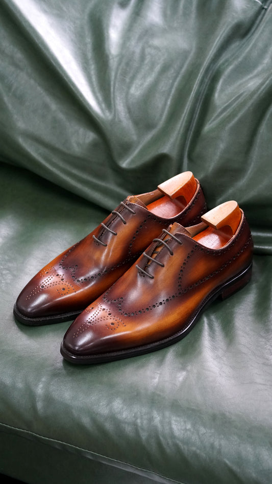 Brown patina leather wholecut Oxford dress shoes with brogue detailing – side view on green leather surface