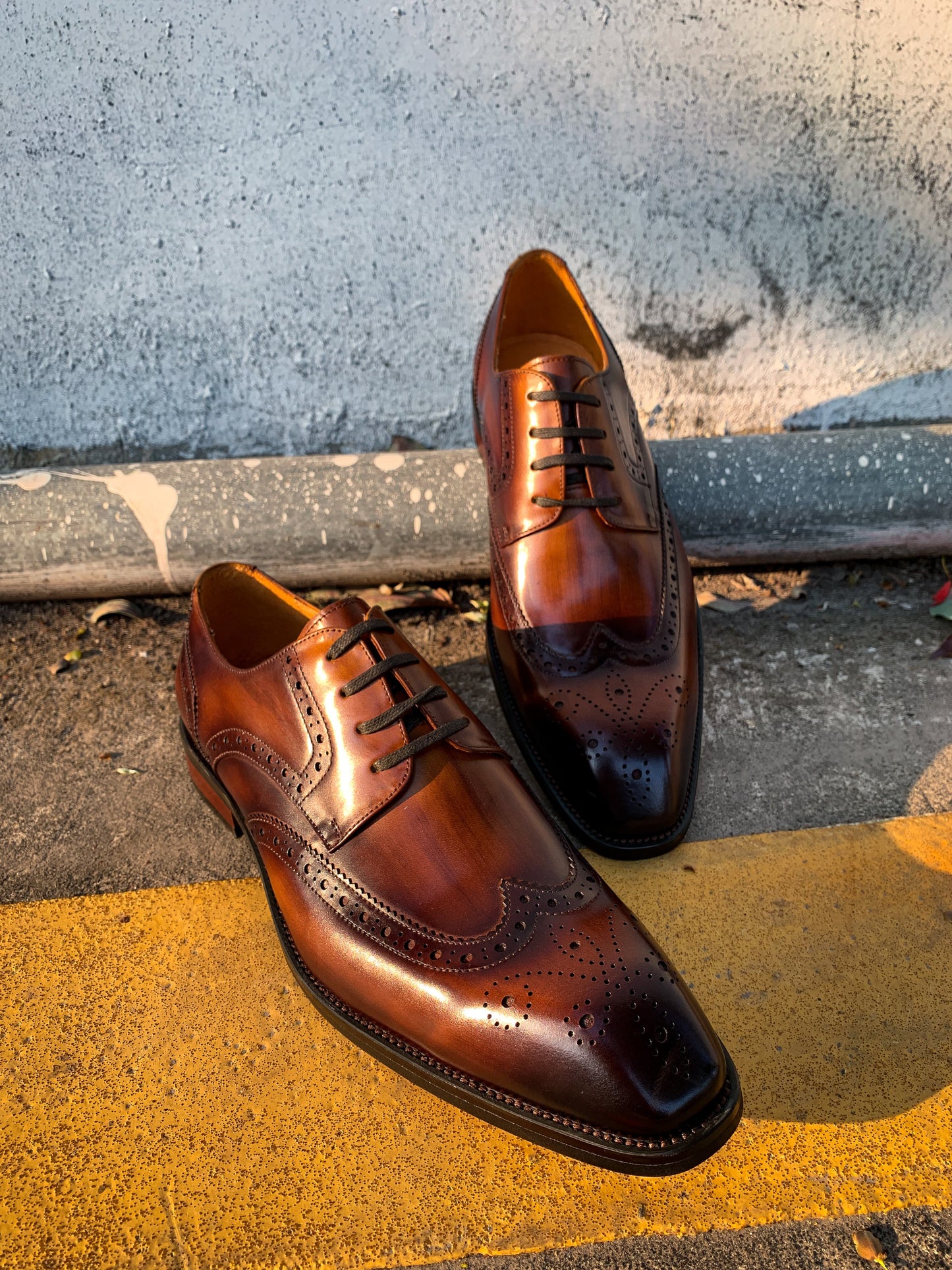 A pair of hand-painted brown and black shaded brogue derby shoes on a yellow-striped pavement.