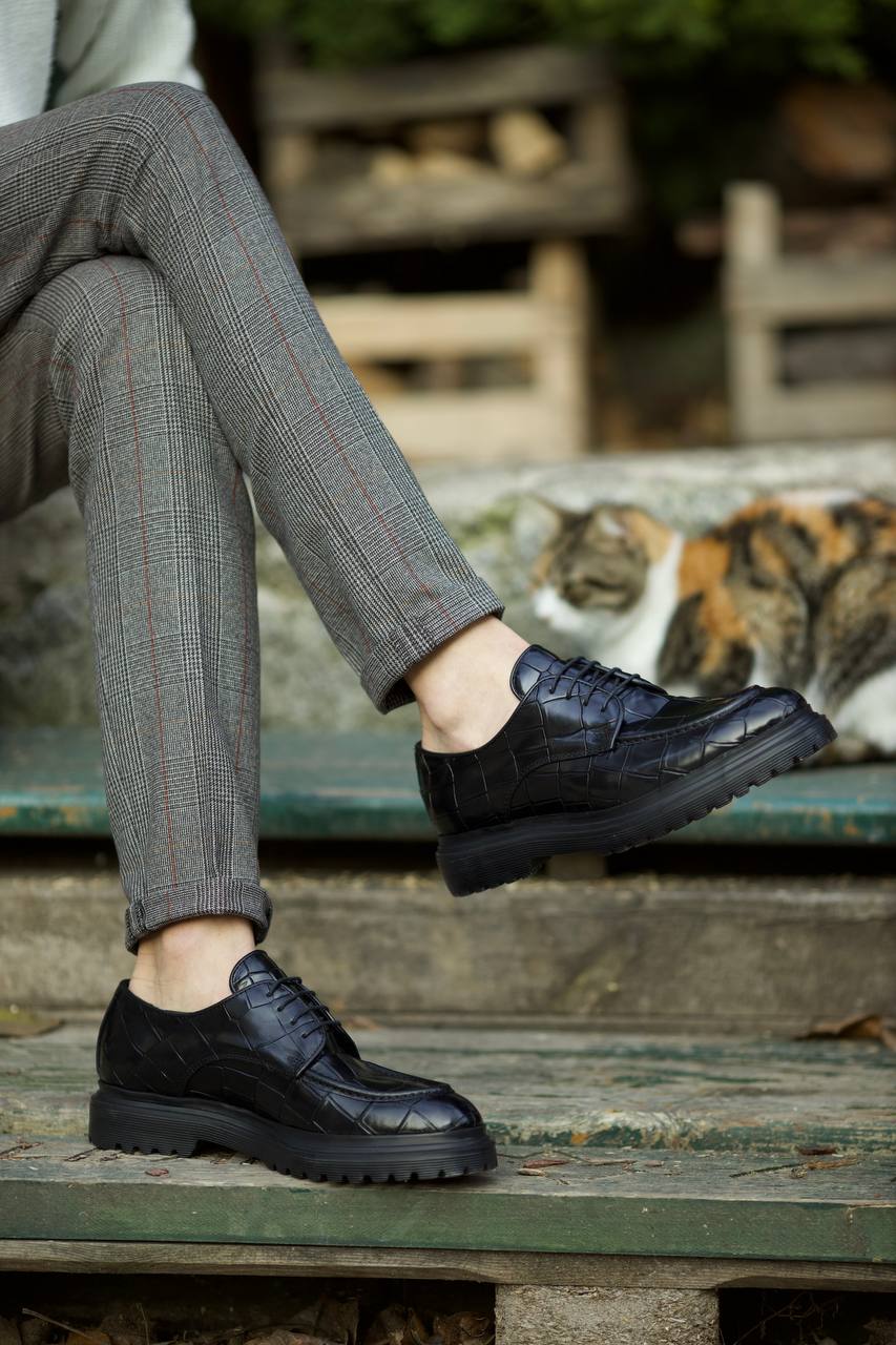 Statement Black Crocodile Leather Derby Shoes – worn by a man in grey plaid trousers, with one foot lifted, highlighting the eye-catching design and comfort.
