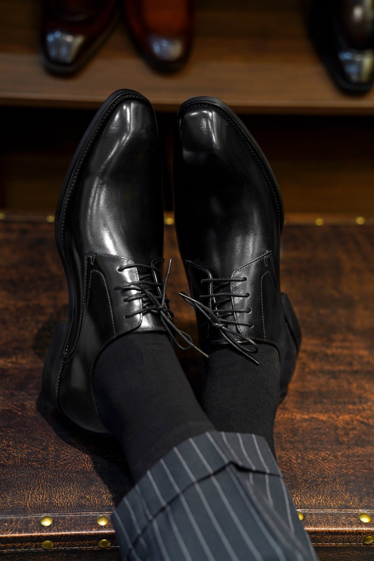 Man wearing Refined Black Derby Shoes – polished black leather, paired with pinstripe trousers, close-up top-down view showcasing timeless design.