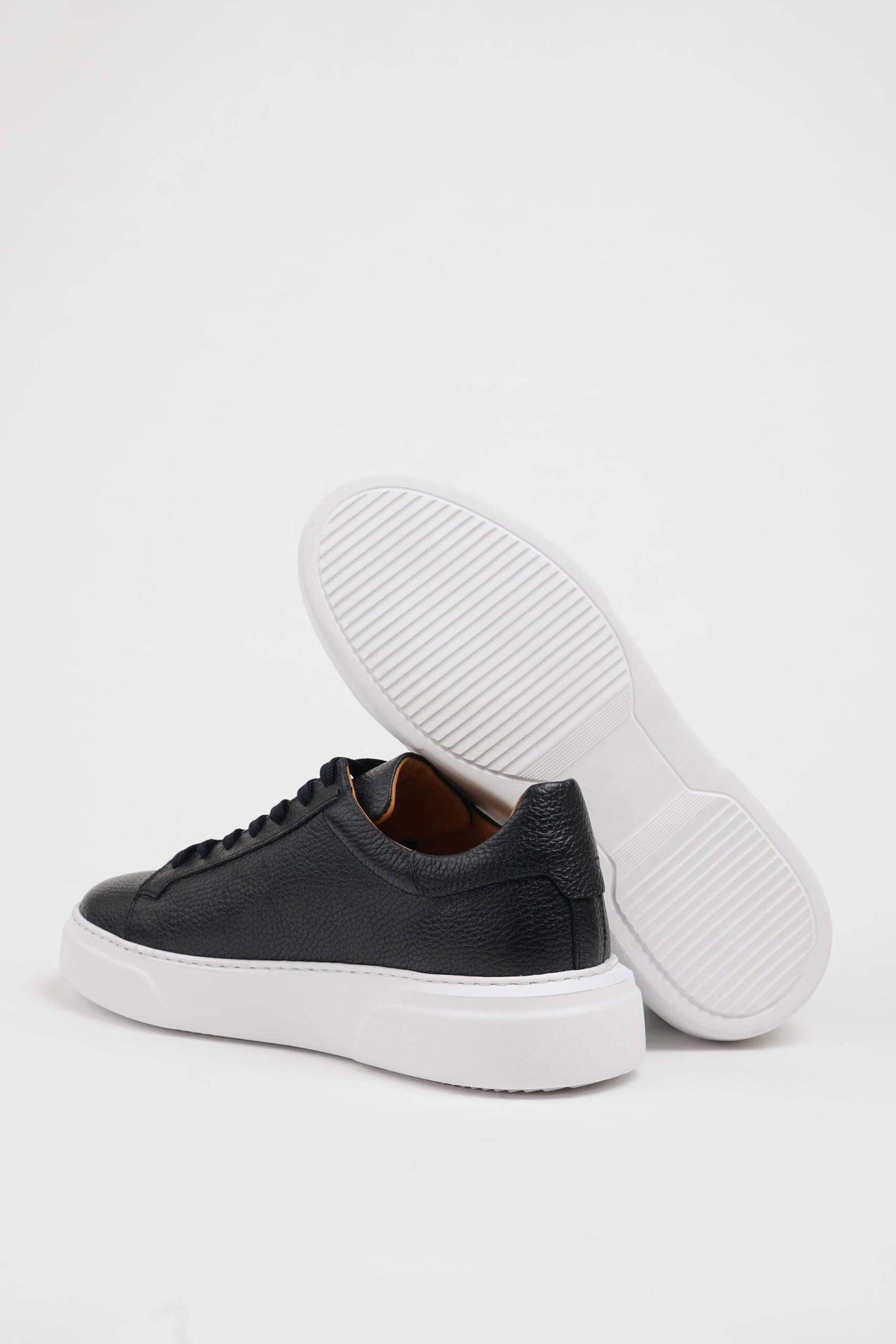 Handcrafted Black Grained Leather Sneakers with Pool Sole – one shoe showing the textured white sole with reliable traction, the other upright.