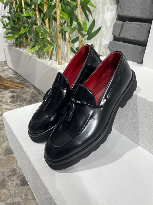 Handcrafted Black Leather Tassel Loafers with Chunky Soles – pair on a white ledge, with red lining, highlighting premium black leather and tassel details.
