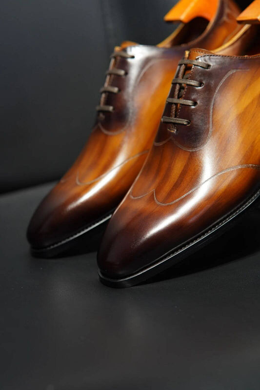 Brown leather oxford dress shoes with a polished patina finish – close-up side view on black surface
