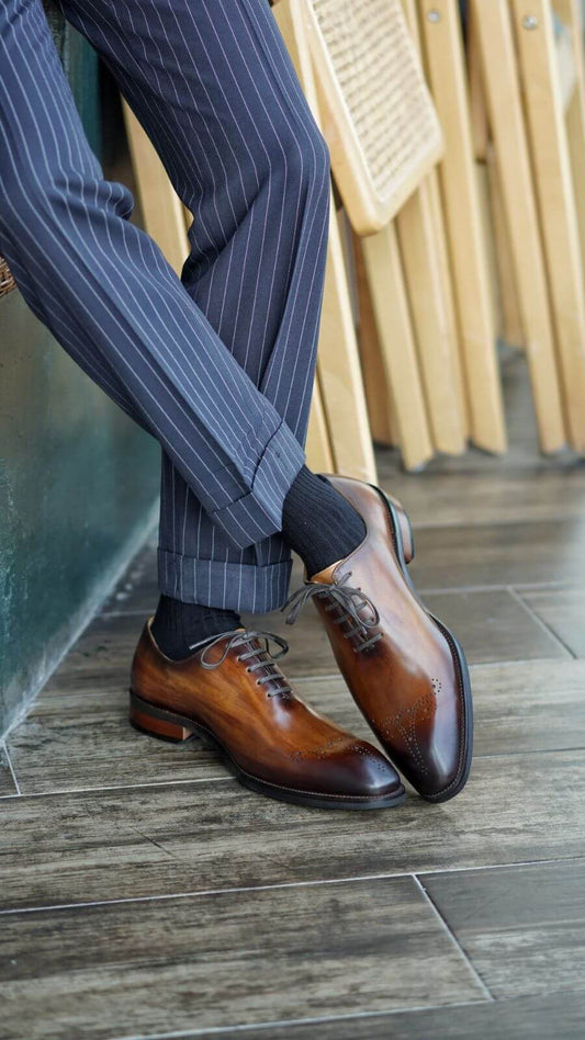 Brown wholecut oxford dress shoes paired with navy pinstripe trousers and black socks – side view with crossed legs.