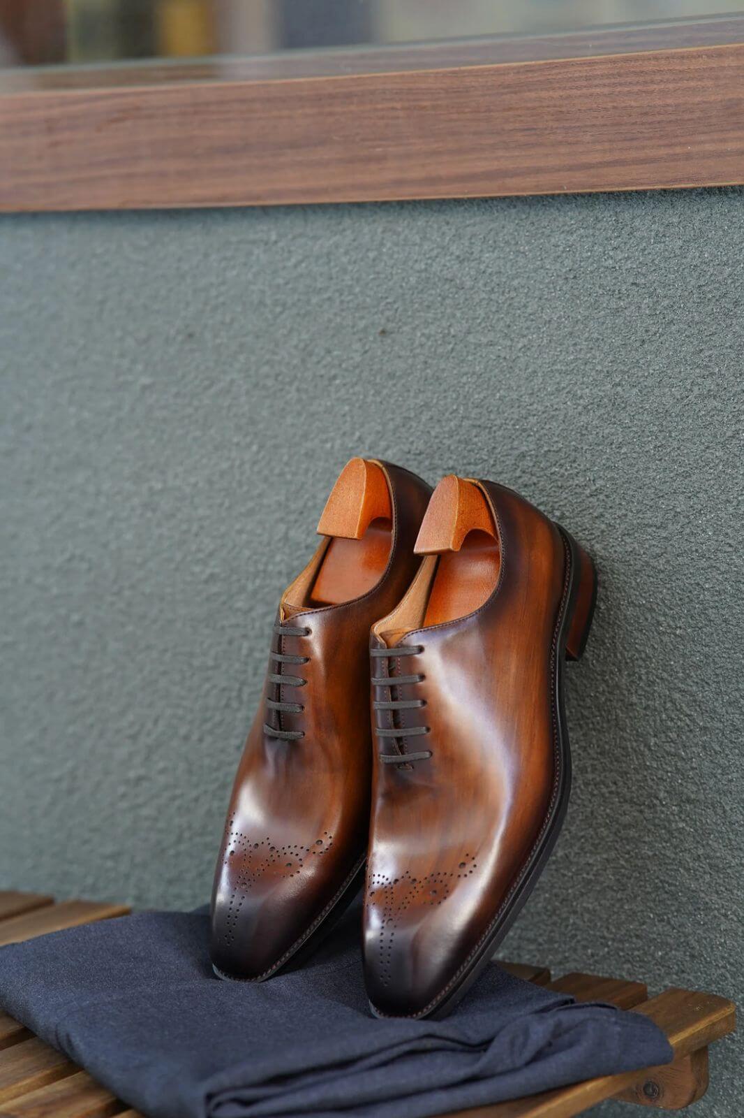 Brown wholecut oxford dress shoes with decorative perforations, displayed with shoe trees on folded navy fabric