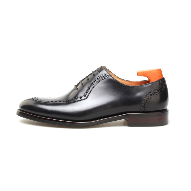 Black leather Oxford brogue dress shoe – angled top-down view with shoe tree on white background.