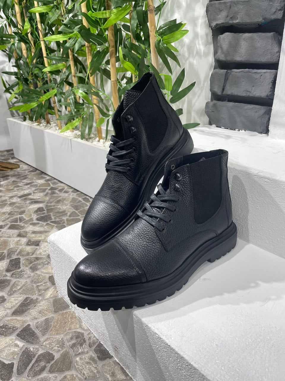 Handcrafted Black Leather Ankle Boots for Urban Style – a pair of black textured leather boots with lace-up details, propped up on white steps.