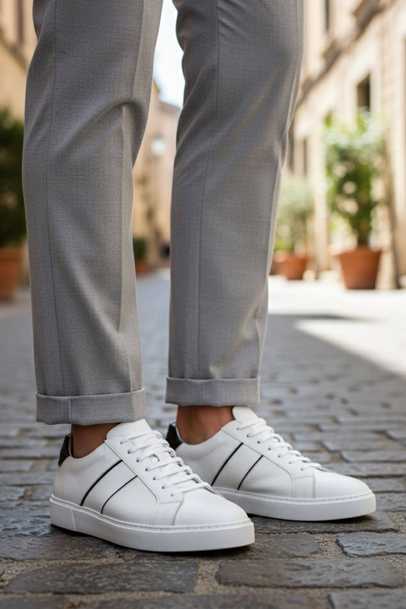 White sneakers worn with gray pants on a stone pavement.