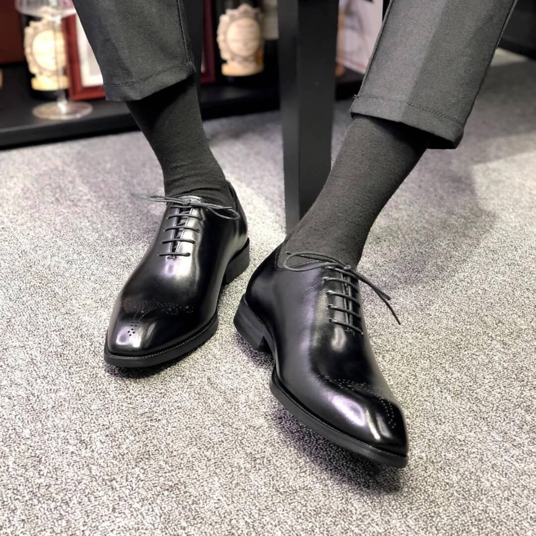Black wholecut oxford dress shoes worn with dark socks – front and side view.