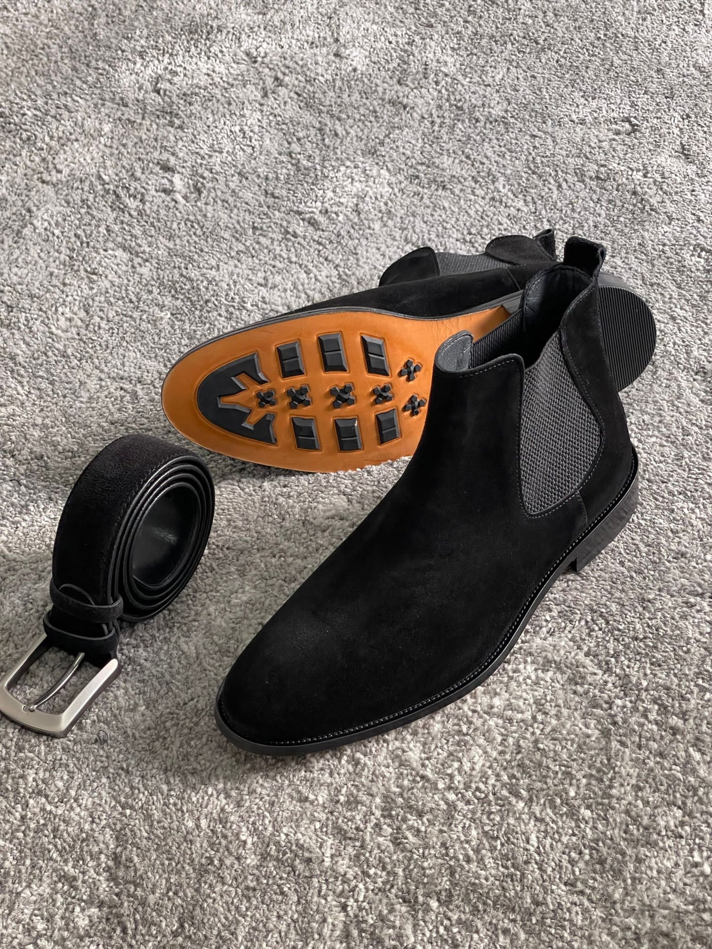 Handmade Classic Black Suede Chelsea Boots – a pair of boots from a high angle, with a belt and socks, featuring a clear view of the unique sole.