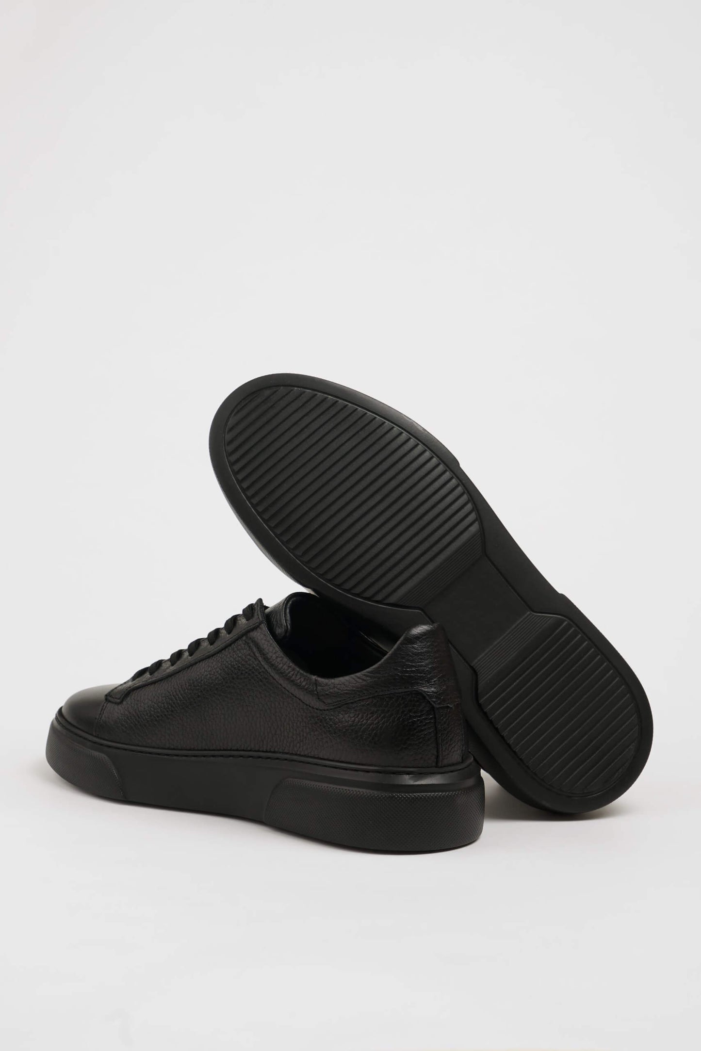 All Black Grained Leather Sneakers for Minimalist Style – one shoe showing the textured black sole for reliable traction, the other upright.