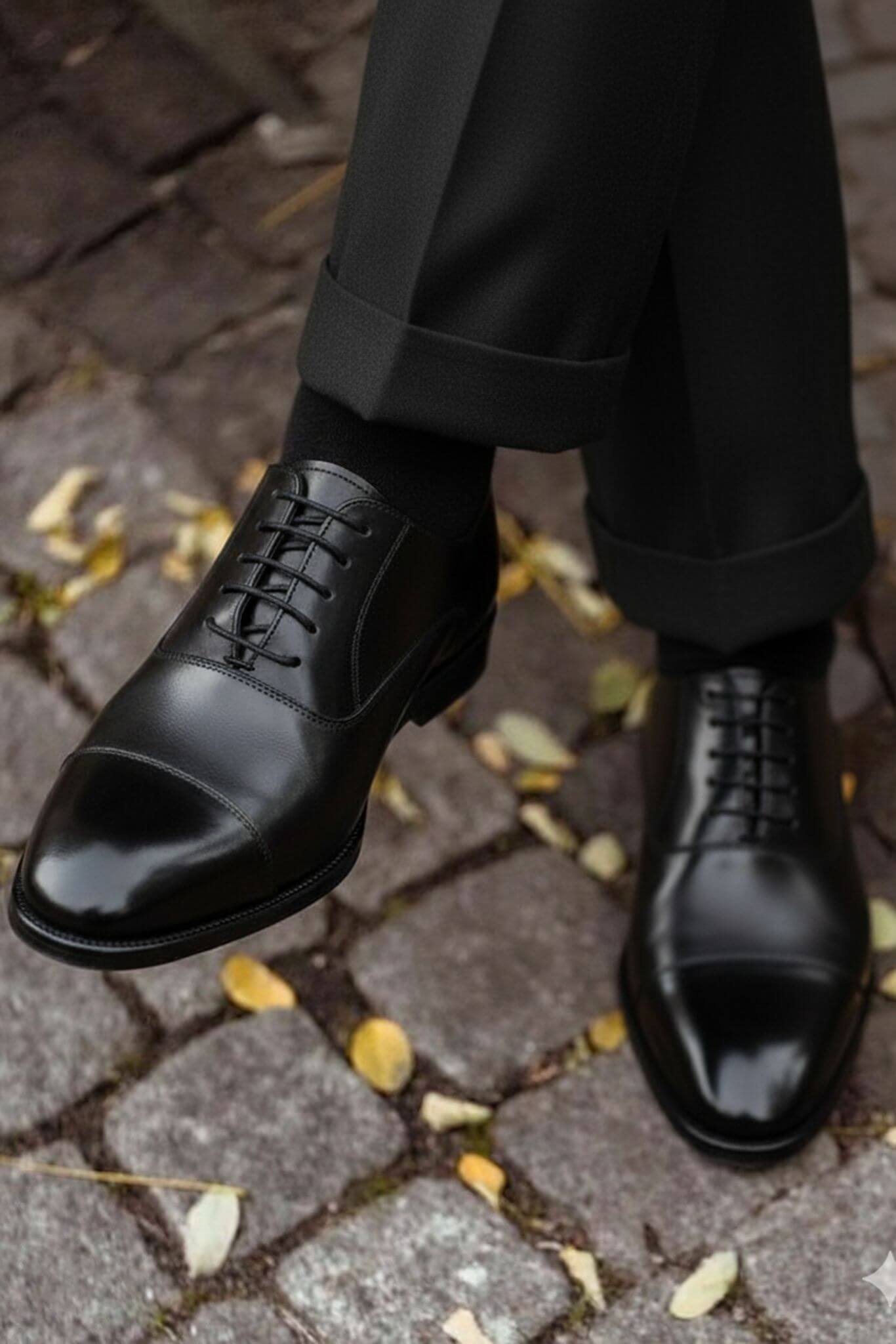 Black leather shoes on a person walking on a cobblestone street with fallen leaves.