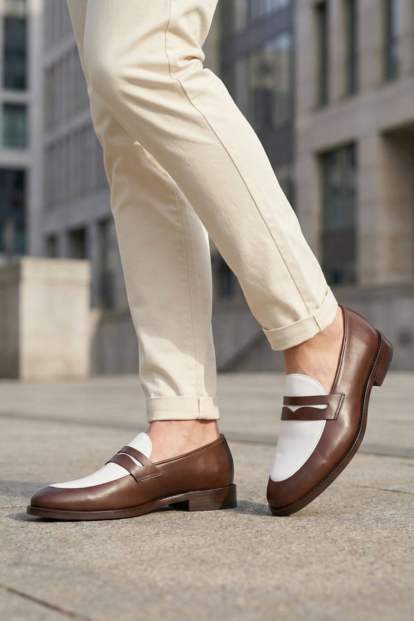 Brown loafers worn with beige pants on a city street.