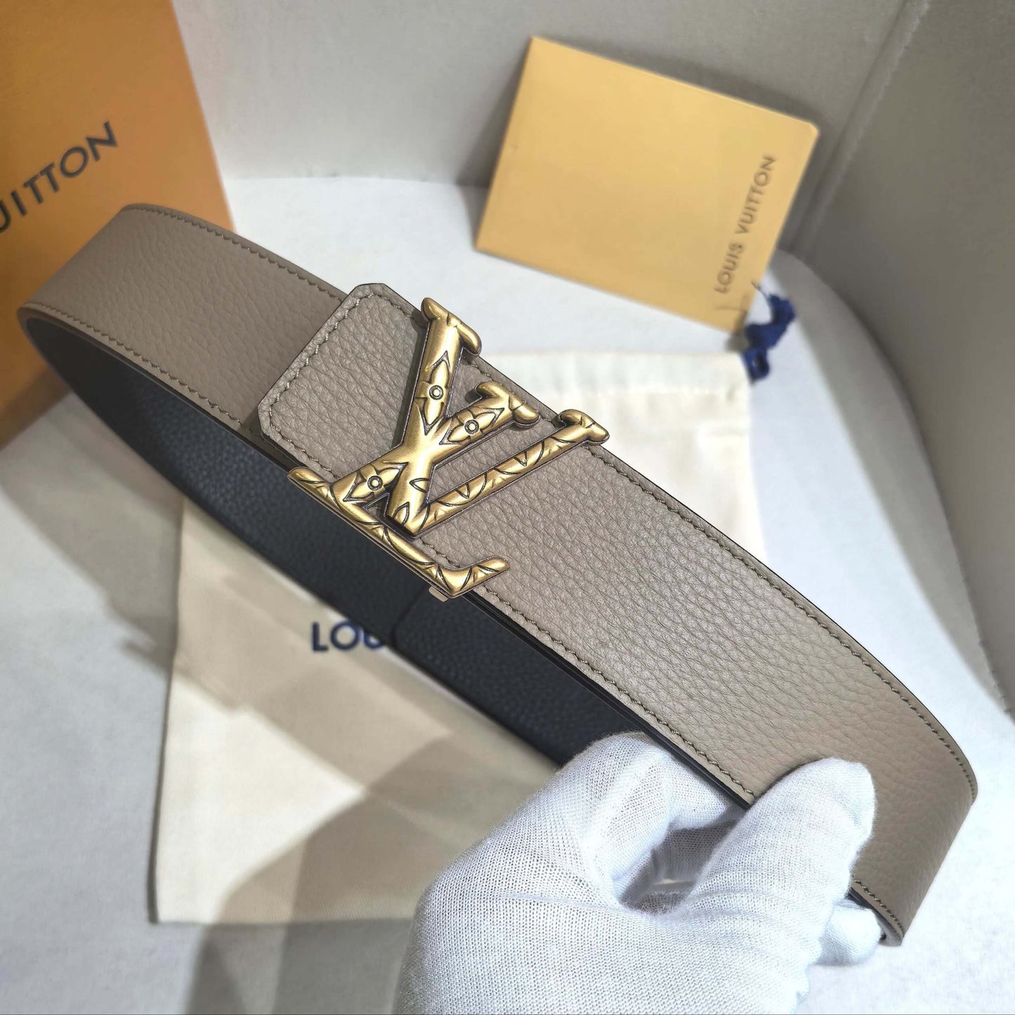 Louis Vuitton belt with gold buckle on a white surface with brand packaging.