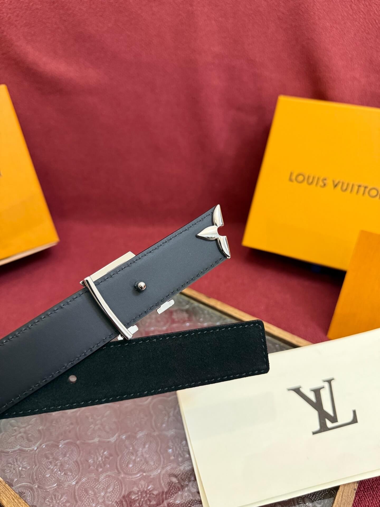 Black belt with silver buckle on a red surface with a Louis Vuitton box and paper.