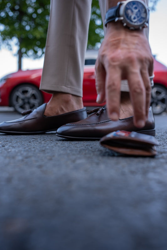 Luxurious Brown Leather Tassel Loafer for Casual & Semi-Formal Wear – worn by a man in tan trousers, bending to pick up a wallet, showcasing the polished leather and refined style.