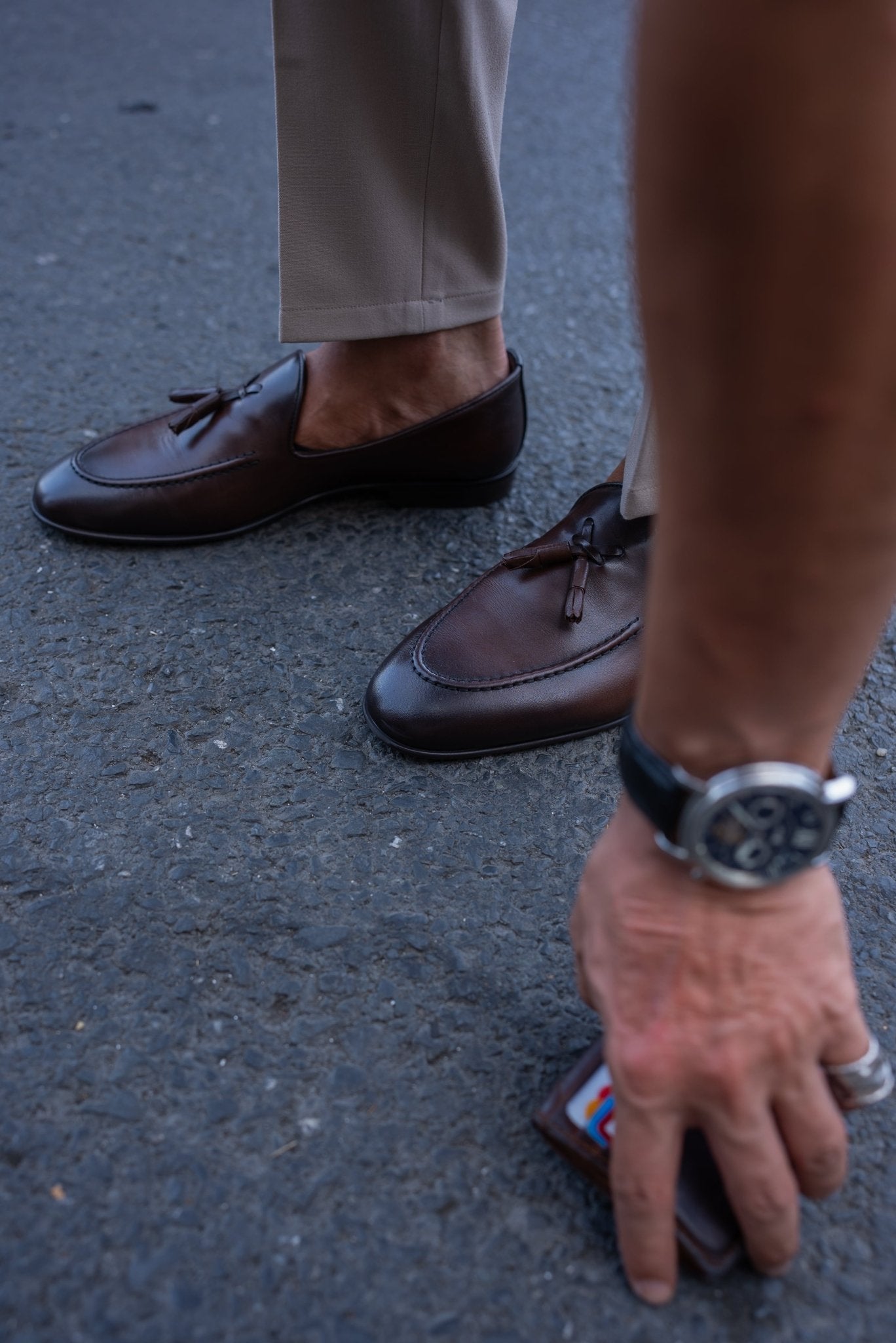 Luxurious Brown Leather Tassel Loafer for Casual & Semi-Formal Wear – close-up of a man's feet in polished leather loafers, bending to pick up a wallet, highlighting craftsmanship and refined tassel detailing.