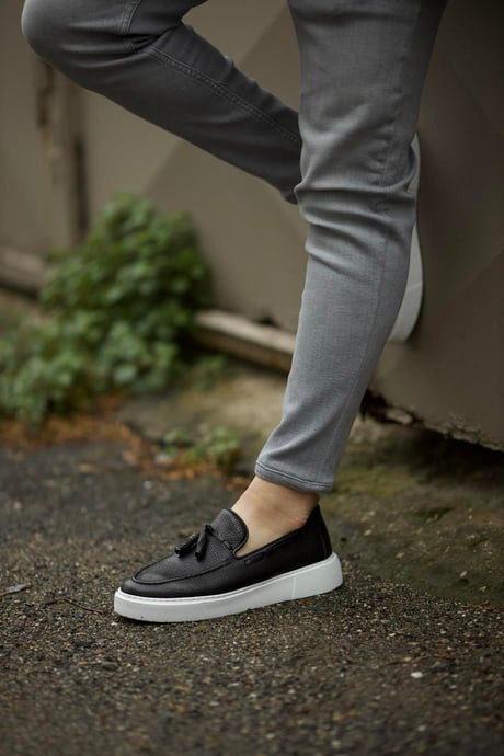 Premium Black Tassel Slip-Ons for Casual & Semi-Formal Wear – worn by a man in grey trousers, leaning against a wall, showcasing a comfortable fit and versatile design.