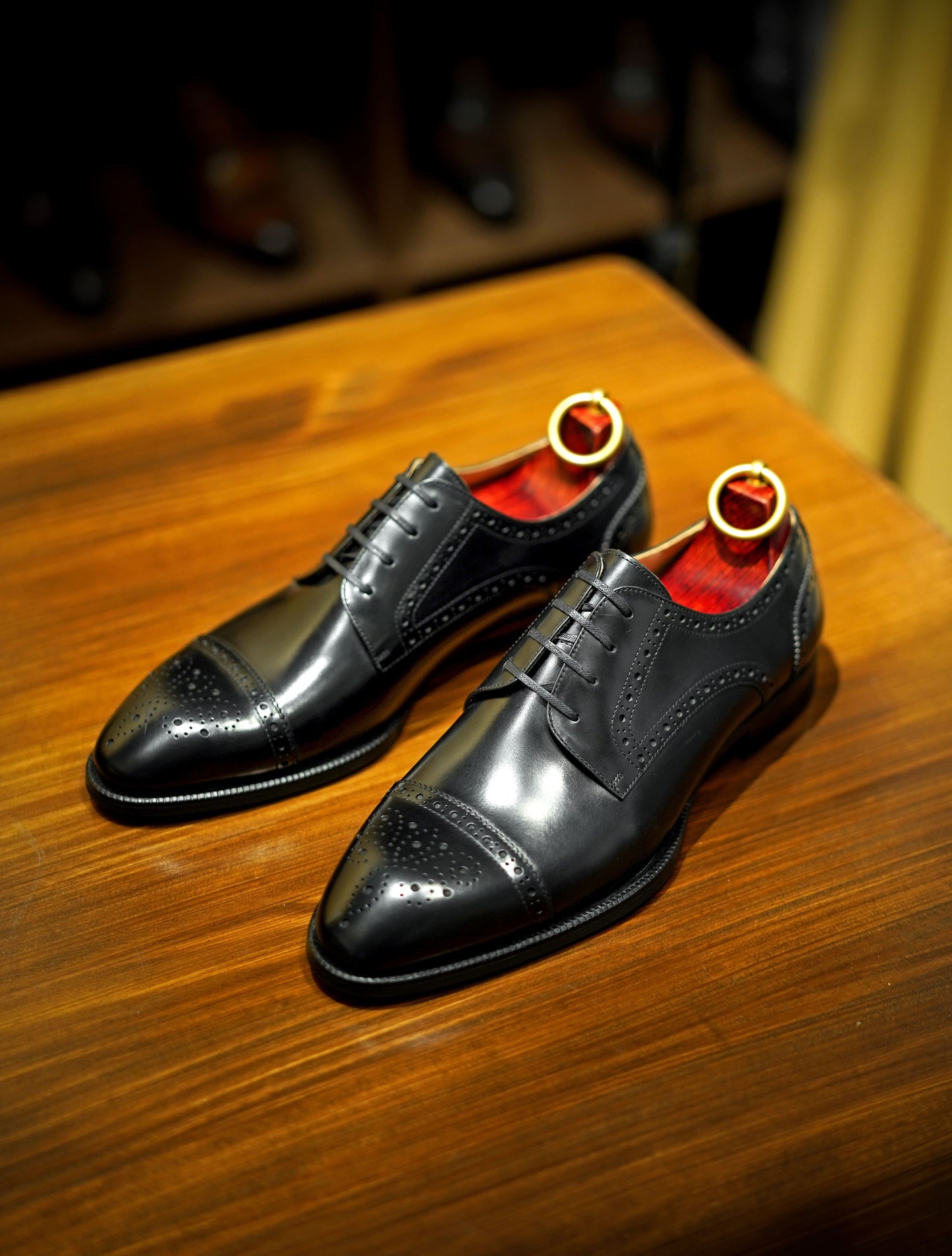 Pair of Refined Black Cap-Toe Brogue Derby Shoes – meticulously crafted from premium leather, displayed on a wooden surface with red lining and shoe trees for formal wear.