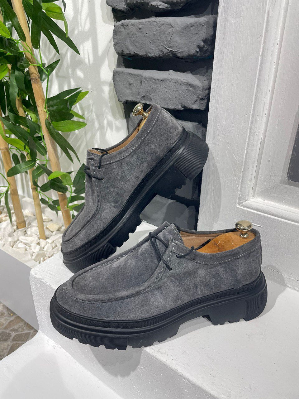 Grey Suede Lace-Up Chunky Shoes – modern design on a white ledge with a brick wall, showcasing contemporary edge and versatile style.