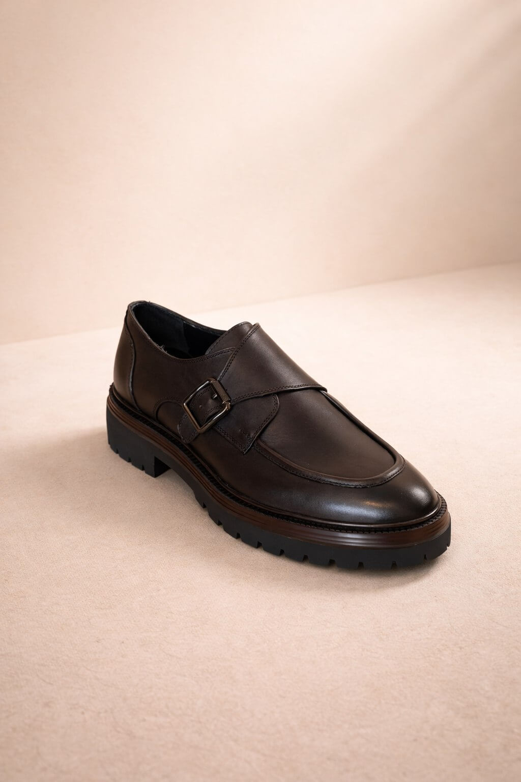 Dark brown leather shoe with a buckle on a beige background