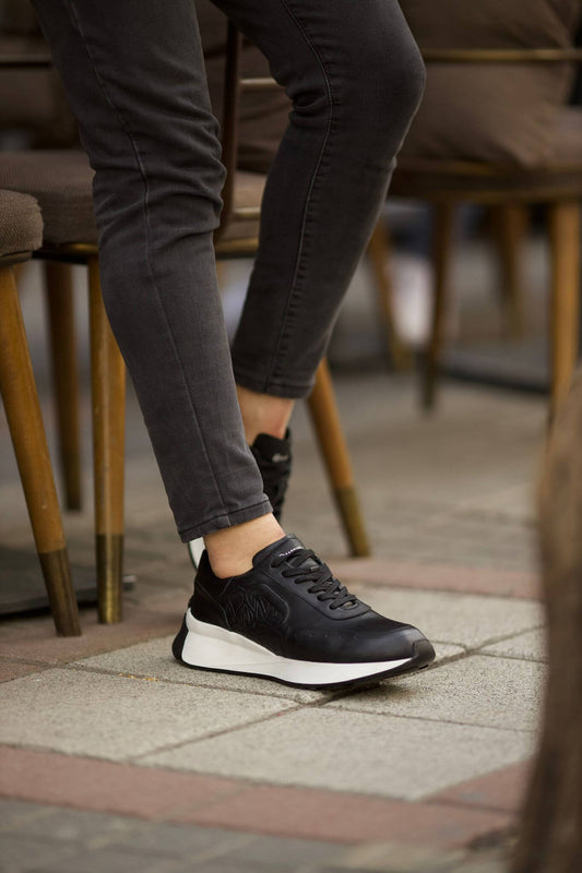 HolloShoe Eva Sole Black Sneakers - Elegant Versatile Footwear – side view, worn by a man in grey jeans, sitting at a table, highlighting the cushioned insole and padded collar.