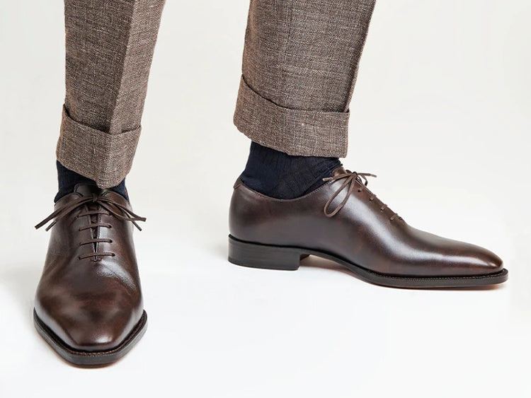 Professional close-up of dark brown wholecut Spanish leather dress shoes worn with textured grey wool trousers.