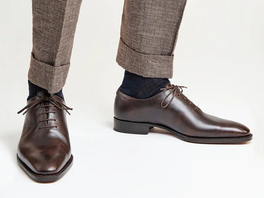 Professional close-up of dark brown wholecut Spanish leather dress shoes worn with textured grey wool trousers.