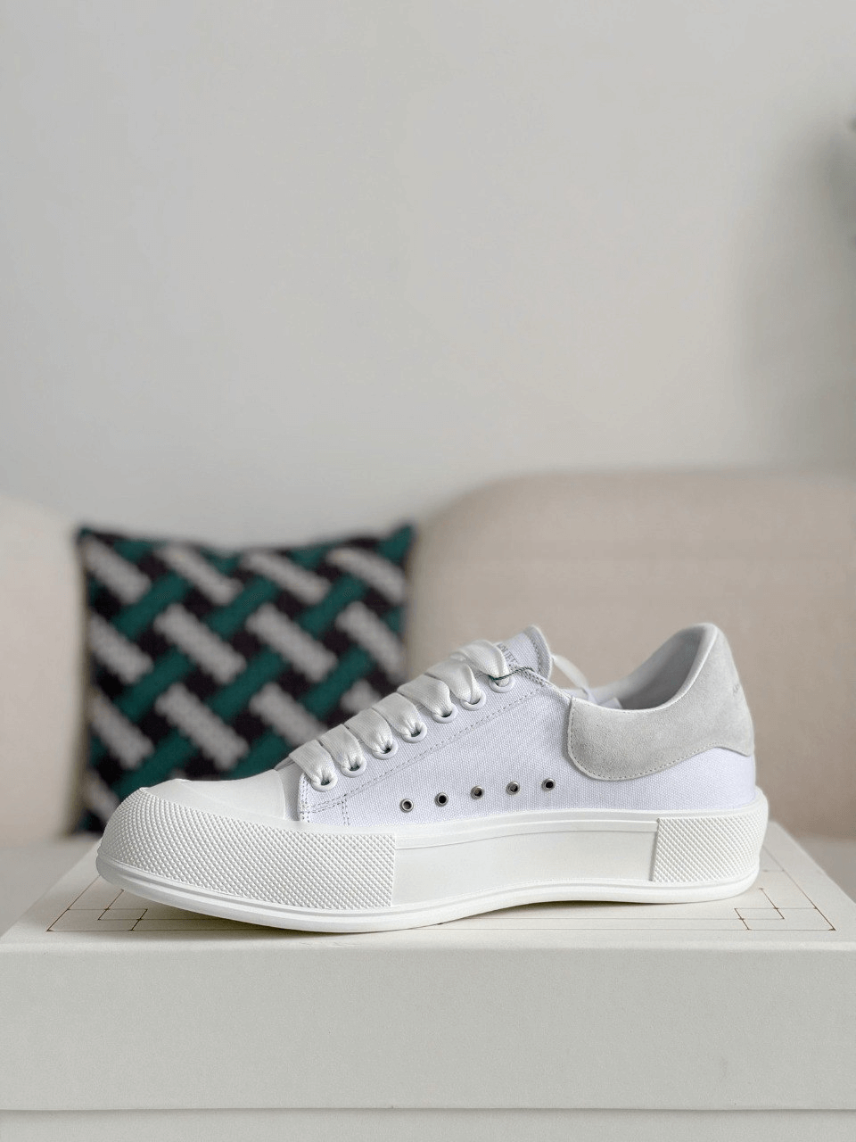 White sneaker on a white surface with a patterned pillow in the background