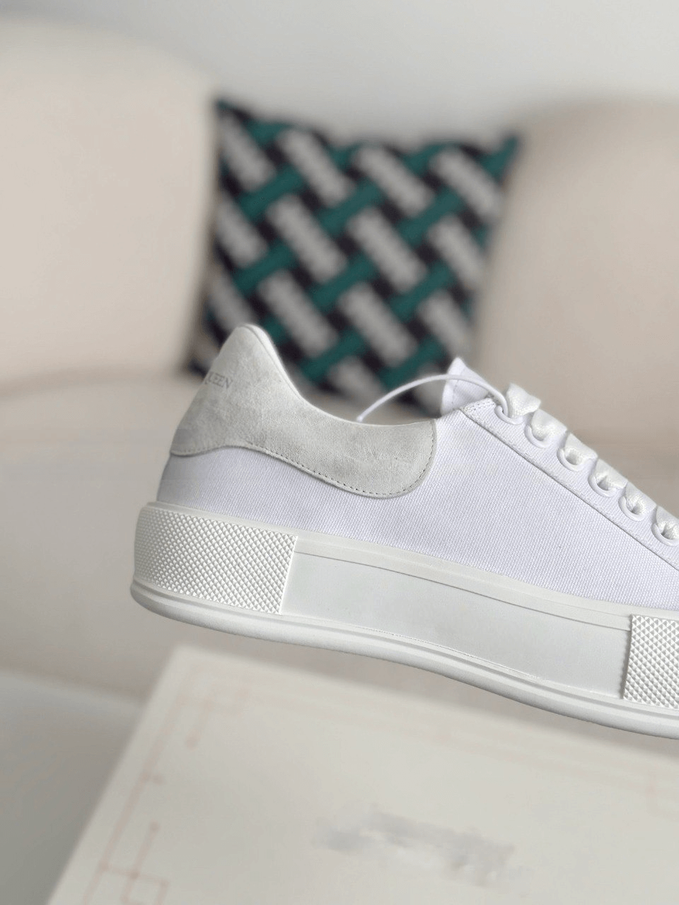 White sneakers on a light-colored surface with a patterned pillow in the background