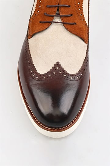Close-up of elegant brogue shoes with brown leather and beige suede accents, showcasing intricate brogue detailing.