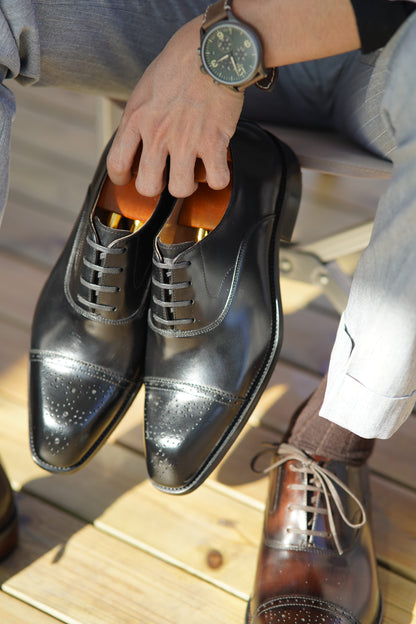 Men's black leather Oxford shoes with a cap toe, brogue detailing, and closed lacing.