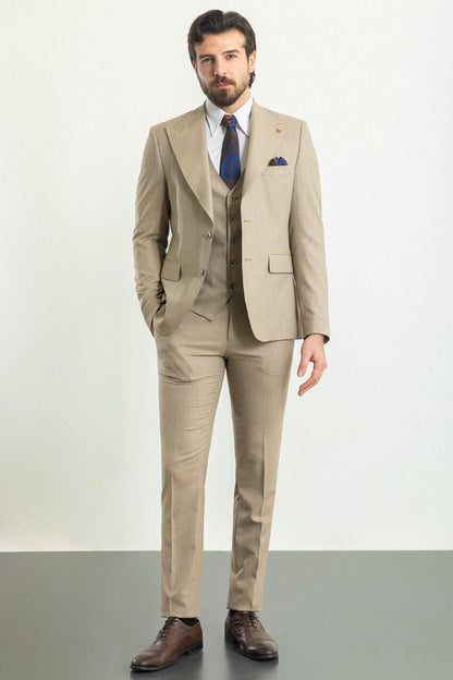 A well-dressed man wearing a Beige 3-Piece Suit stands confidently in a studio setting. The suit is paired with a white dress shirt, a patterned tie, and a matching pocket square, adding a refined touch to the ensemble. Brown leather dress shoes complement the outfit, enhancing its classic elegance. The man has neatly styled hair and a trimmed beard, projecting a polished and sophisticated look, ideal for formal and professional occasions.