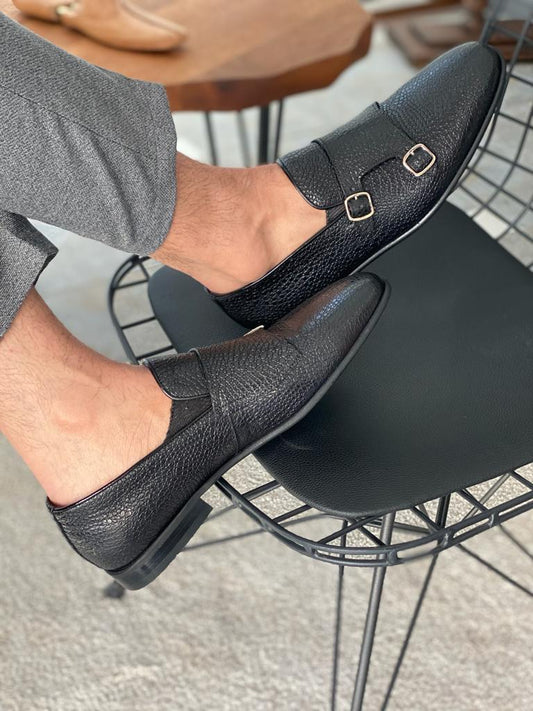 Black Grained Leather Double Monk Strap Shoes – worn by a man in grey trousers, resting on a black chair, highlighting textured leather and comfortable fit.