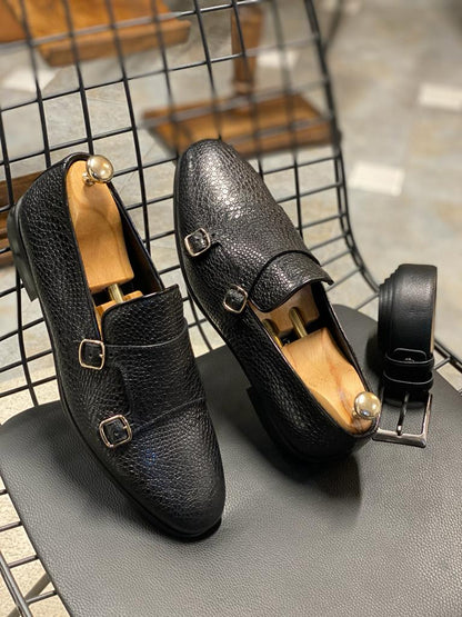 Black Grained Leather Double Monk Strap Shoes – pair with shoe trees and matching black belt on a chair, highlighting pebbled texture and buckles.