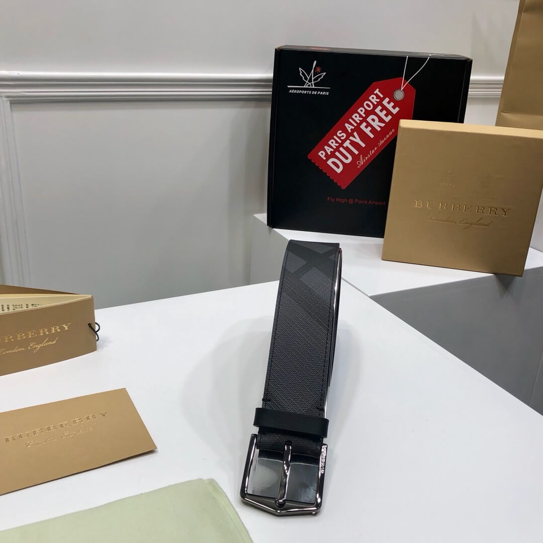 Black belt with silver buckle on a white surface, surrounded by Burberry packaging.