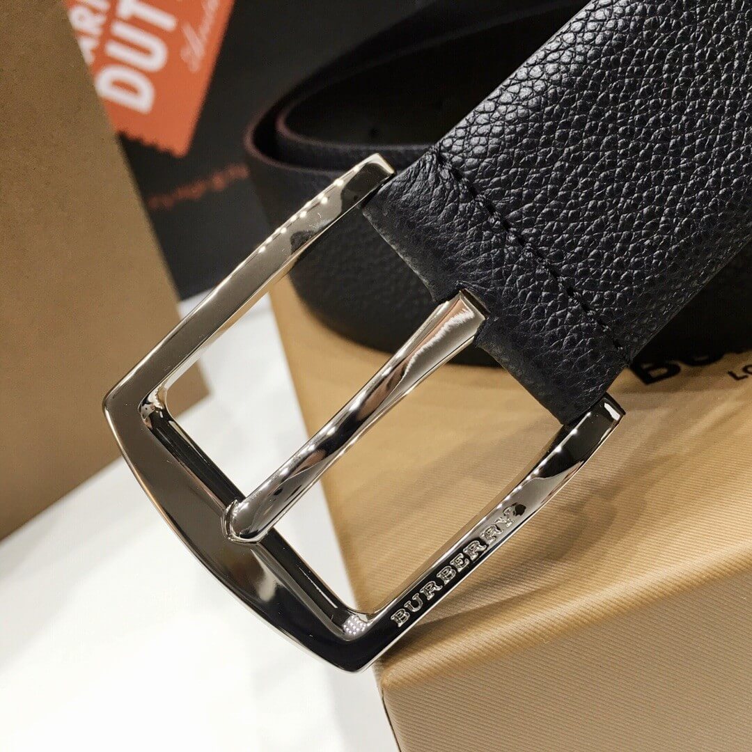 Close-up of a black leather belt with a silver buckle on a beige surface.