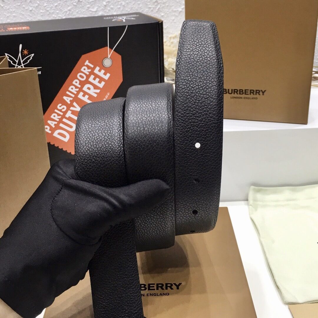 Black leather belt held by a gloved hand with Burberry branding in the background.