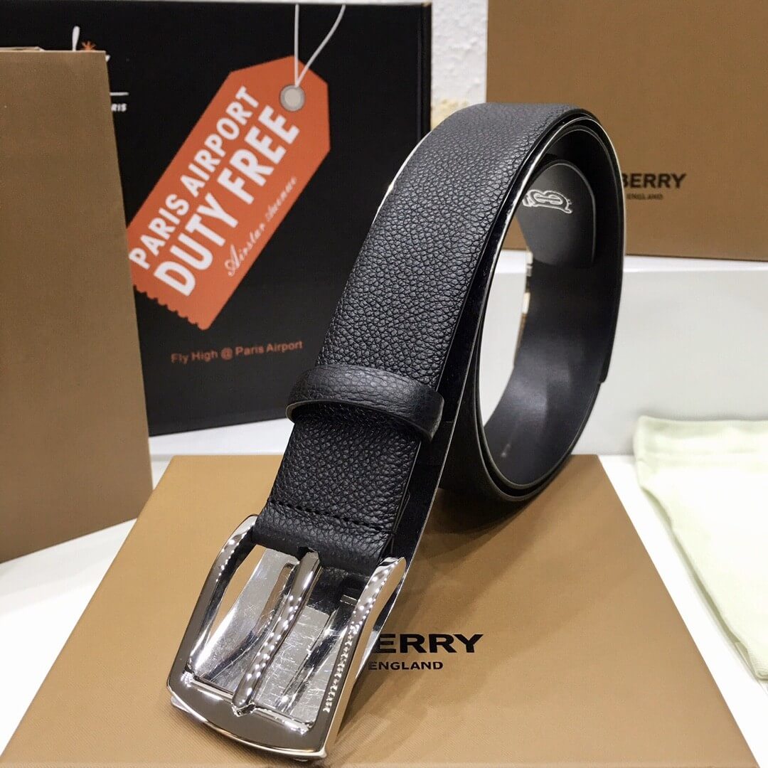 Black leather belt with silver buckle on a brown surface, with 'Paris Airport Duty Free' tag in the background.