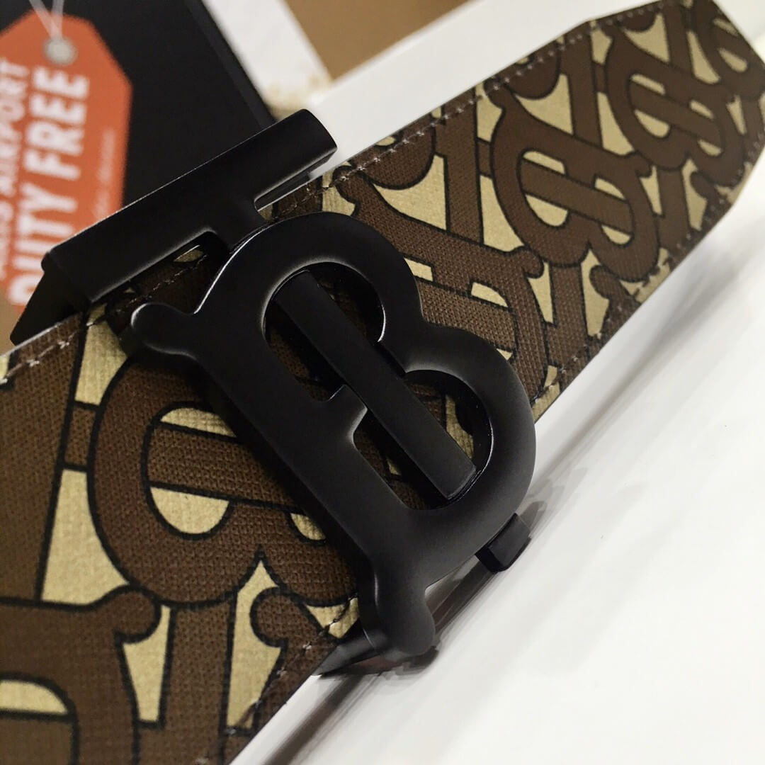 Close-up of a black belt buckle with a brand logo on a patterned fabric background.