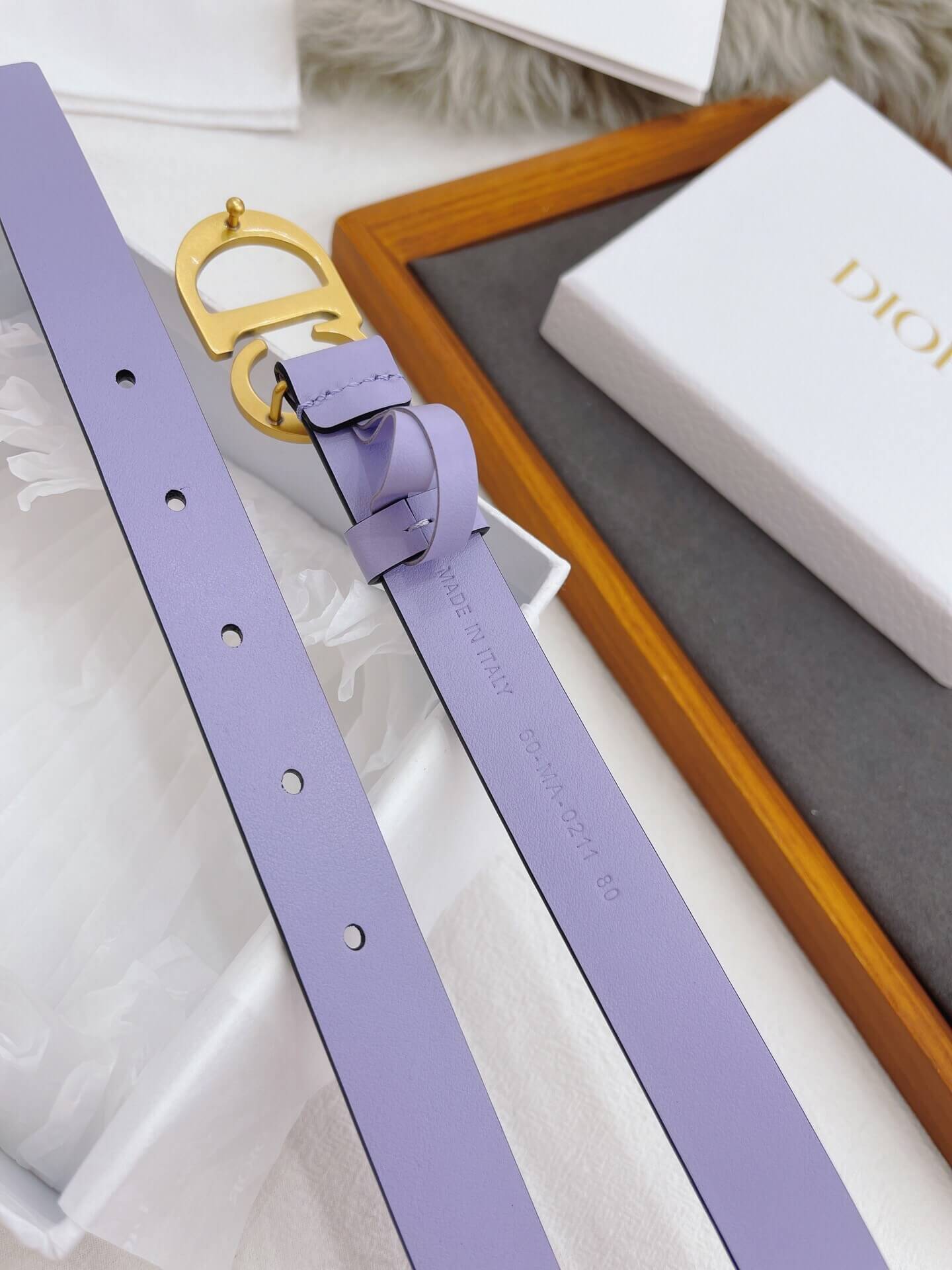 Purple belt with gold buckle on a textured surface next to a Dior box.