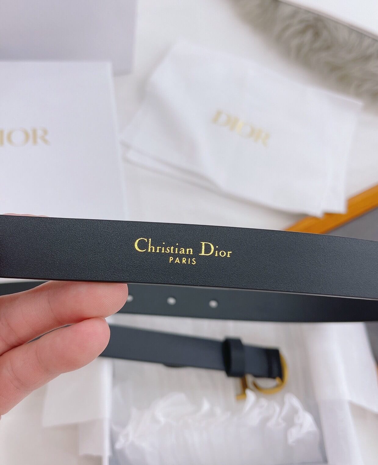 Christian Dior belt with gold text held by a hand against a blurred background