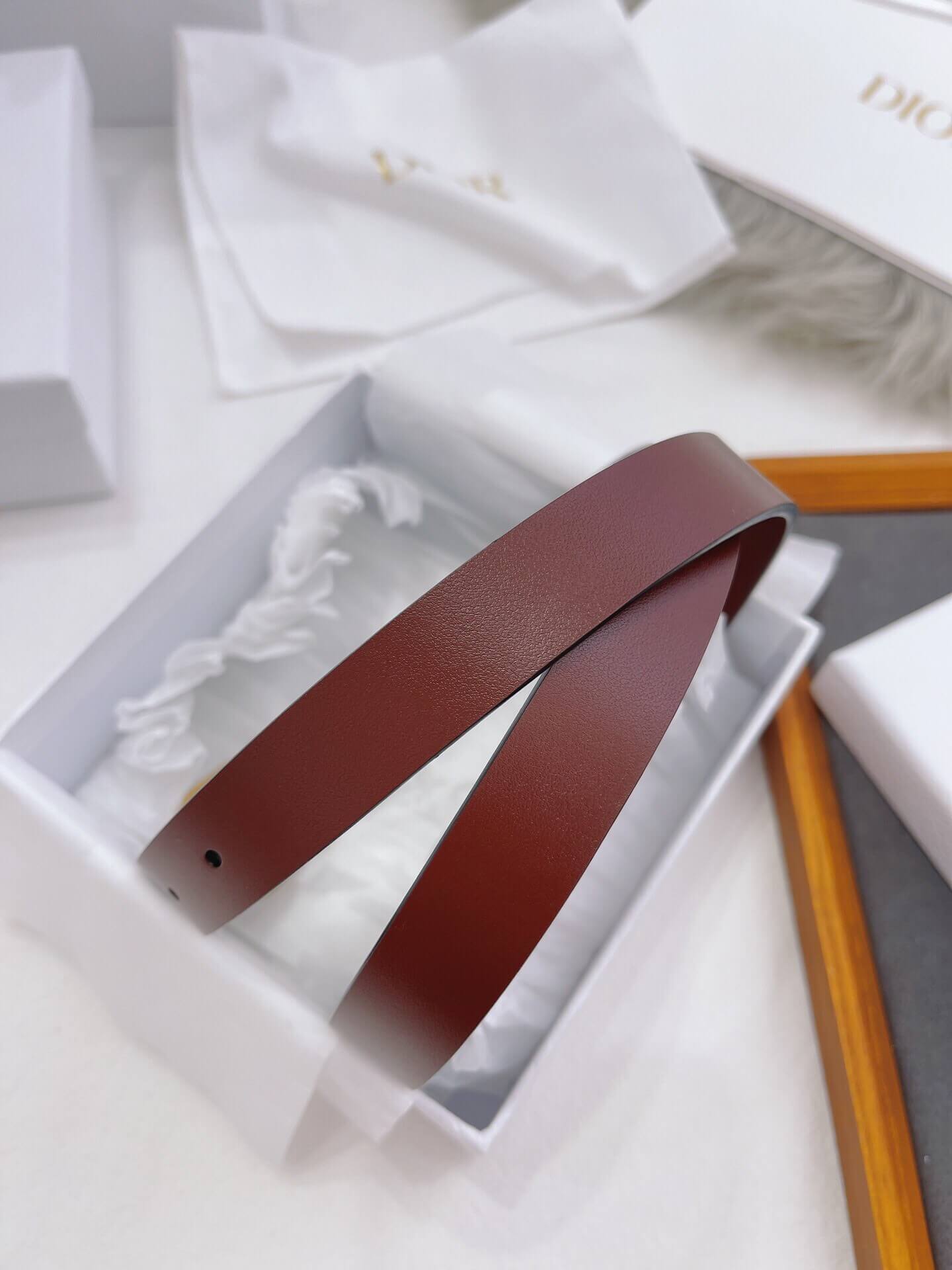Brown leather belt in a white box with 'Dior' branding in the background.