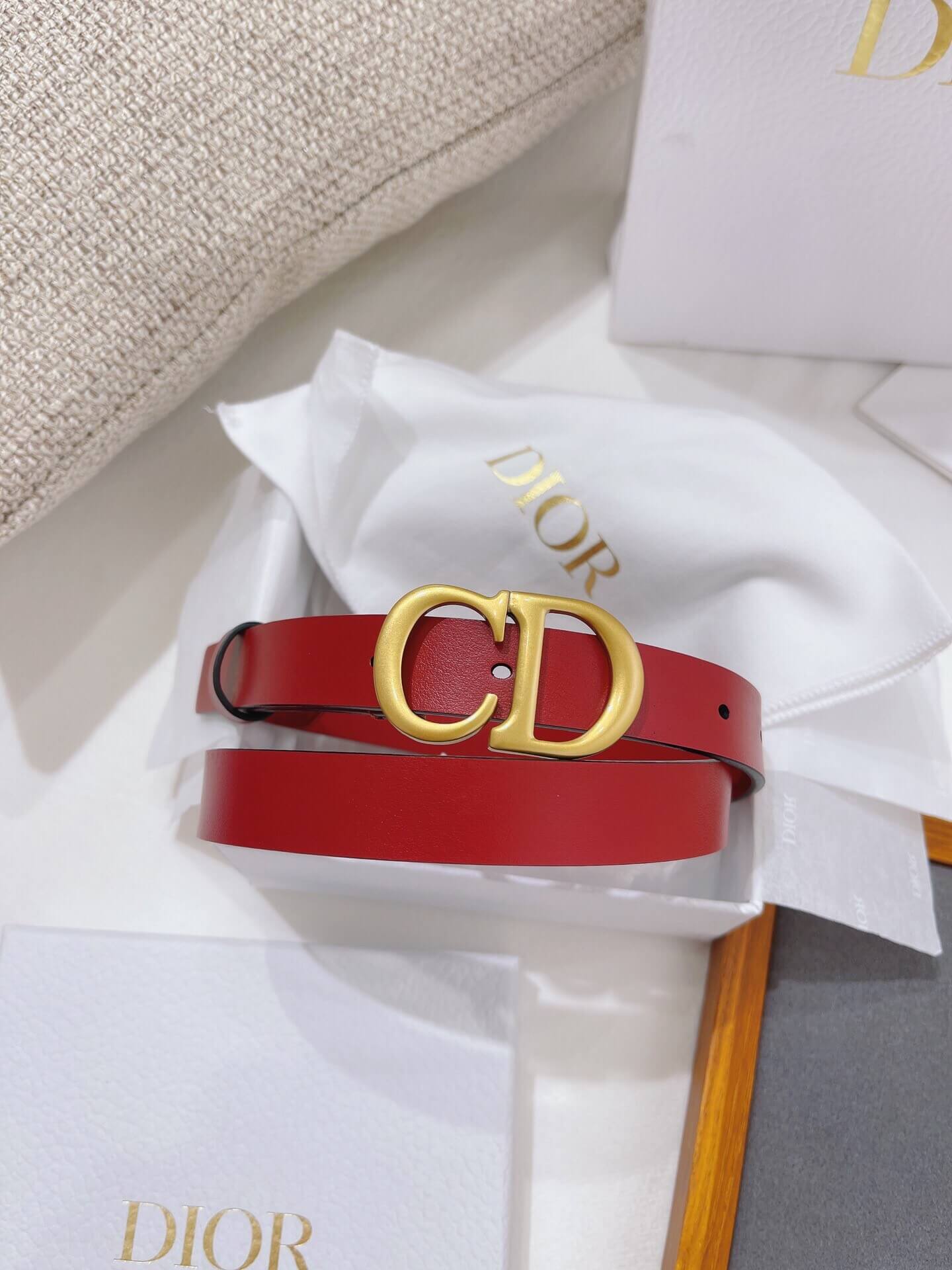 Red Dior belt with gold buckle on a white ribbon against a neutral background