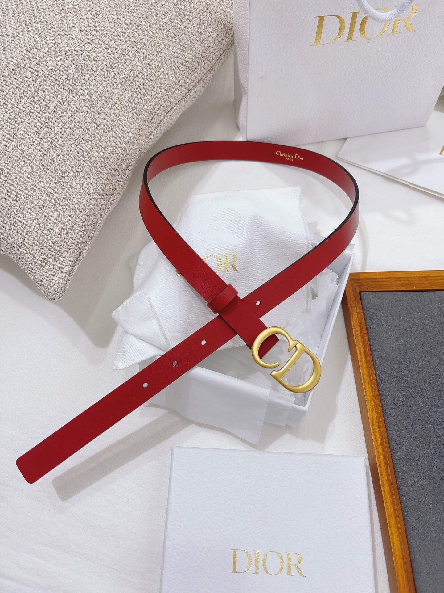 Red belt with gold Dior buckle on a white surface with Dior branding.