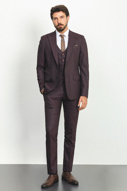 A well-groomed man wearing a Burgundy Checkered Three-Piece Suit stands confidently in a studio setting. The suit features a rich burgundy color with a subtle checkered pattern, paired with a white dress shirt, a patterned tie, and a matching pocket square, adding a refined touch to the ensemble. Brown leather dress shoes complement the outfit, enhancing its classic elegance. The man has neatly styled hair and a trimmed beard, projecting a sophisticated and polished look ideal for formal occasions.