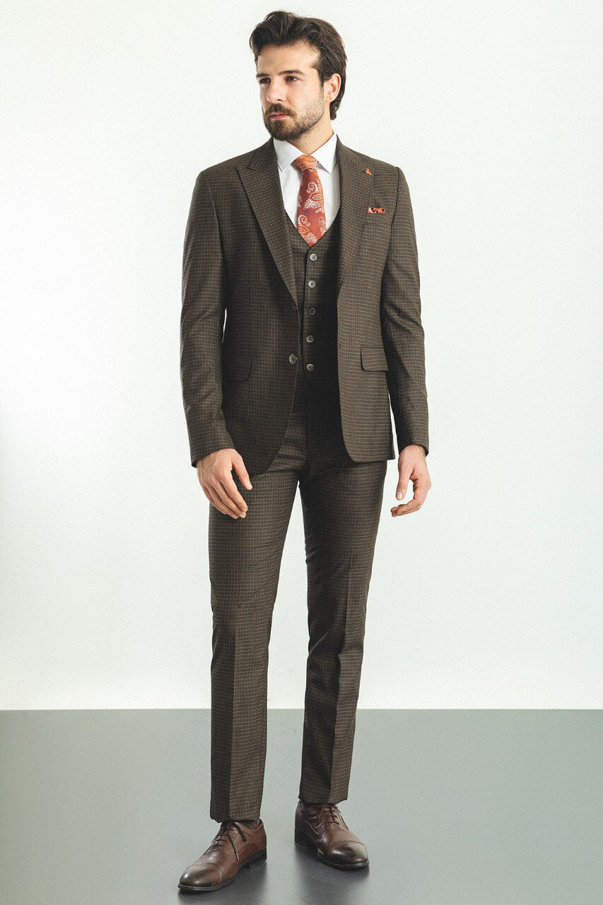 A well-dressed man wearing a Brown Checkered Three-Piece Suit stands confidently in a studio setting. The suit features a subtle checkered pattern, paired with a white dress shirt, a vibrant red paisley tie, and a matching pocket square, adding a touch of sophistication. The ensemble is completed with brown leather dress shoes, exuding classic elegance. The man has neatly groomed hair and a trimmed beard, embodying a polished and refined look perfect for formal occasions.