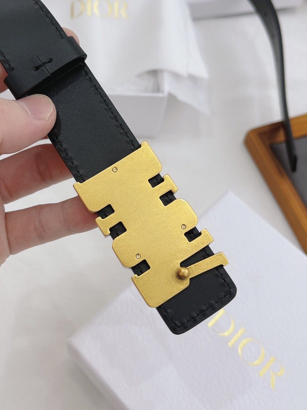 Black belt with gold buckle held by a hand on a white background